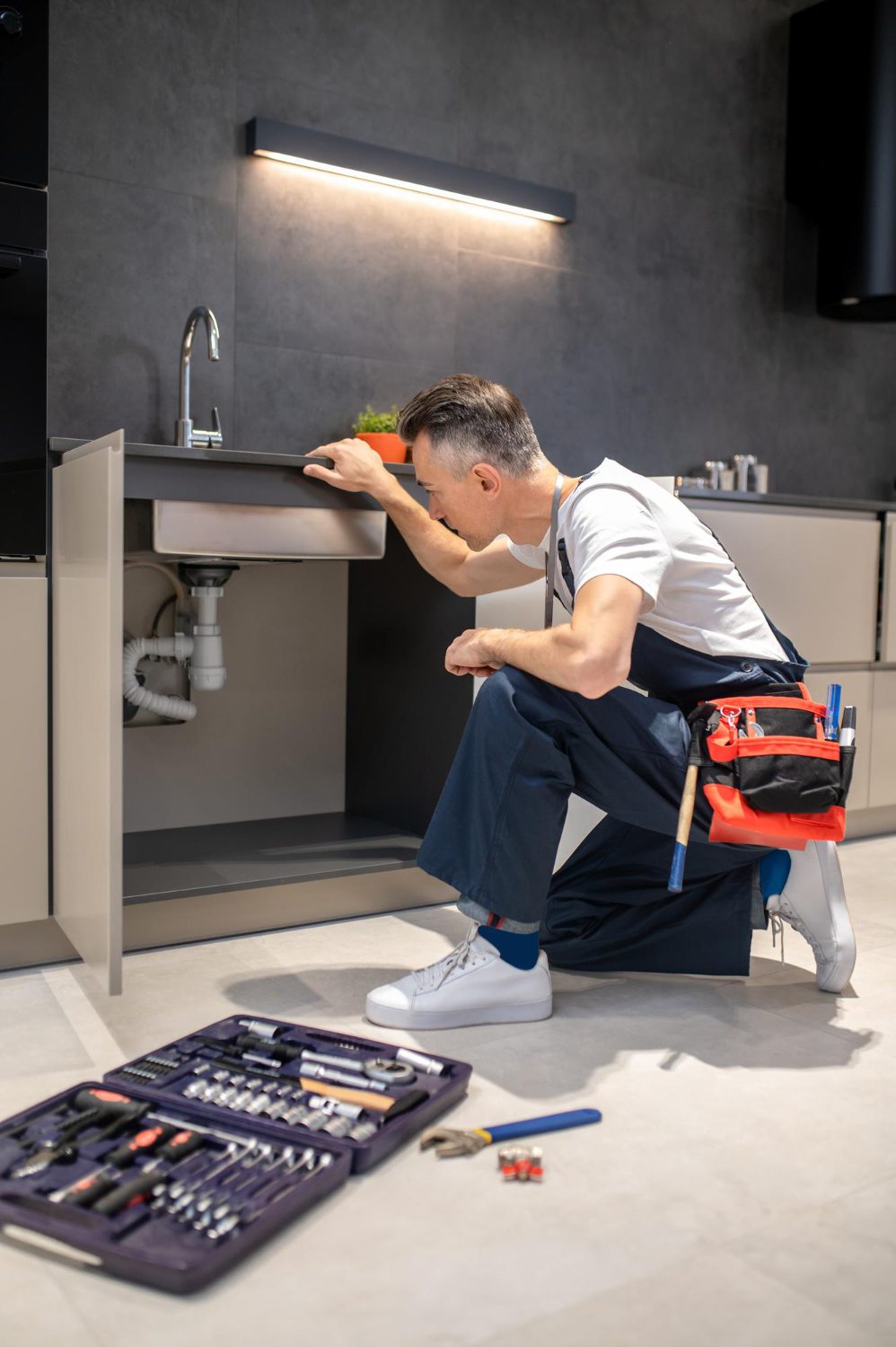 Man kneeling down touching sink inspecting pipes Man kneeling down touching sink inspecting pipes